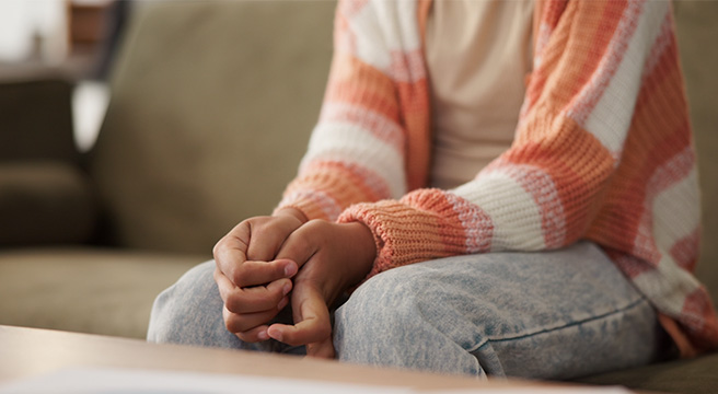 Photo: Young person seated on sofa wringing hands
